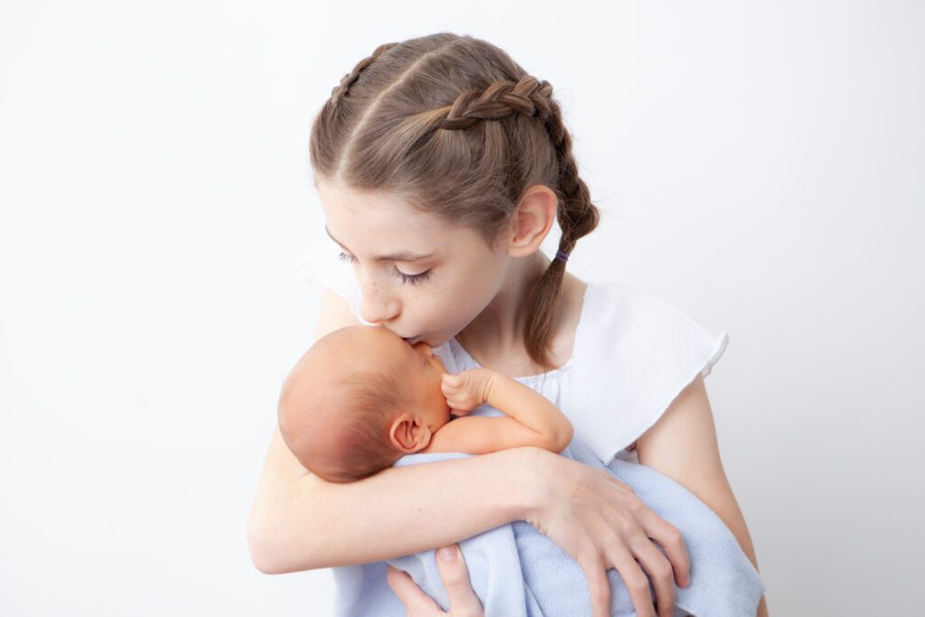 big sister kisses newborn baby at newborn photo session in Portland Oregon photography studio